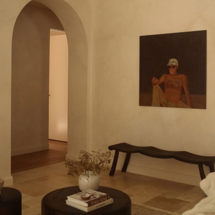 Living room with a painting on the wall, a bench, and a small table with books and a vase.